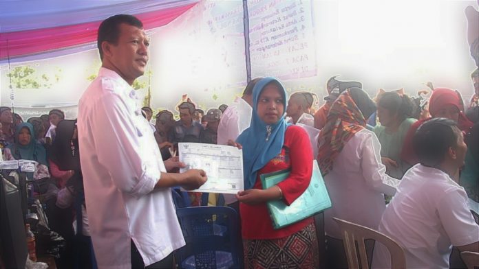 Yudha Triwidya Sasongko, Kepala Dispendukcapil Kabupaten Pasuruan menyerahkan Kartu Keluarga kepada seorang warga dalam layanan Kendaraan Urun Rembuk Masyarakat di Lapangan Pasrepan, beberapa waktu lalu.